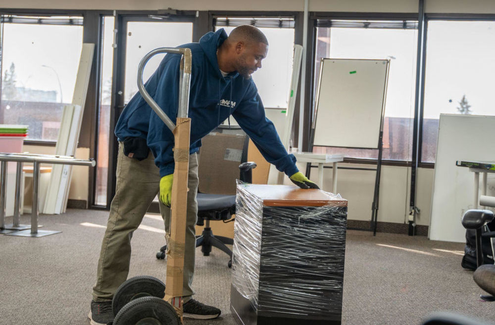 Mover using a dolly to move a wrapped piece of furniture in an office